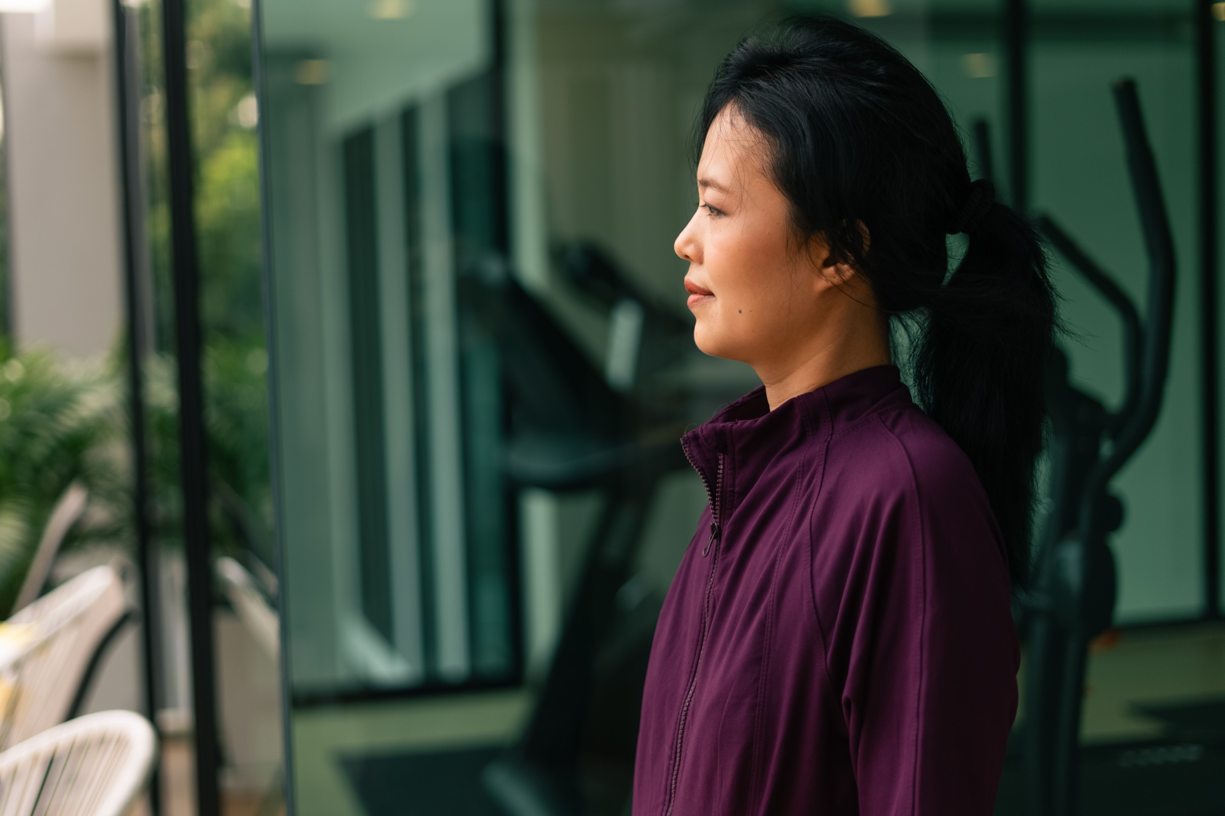 asian-woman-taking-break-from-workout-contemplating-modern-gym-setting.jpg